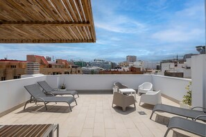 A rooftop terrace with lounge chairs, a table, and a view of the cityscape. - Guestready - Nuevos Livian Suites Las Palmas (Las Palmas de Gran Canaria)