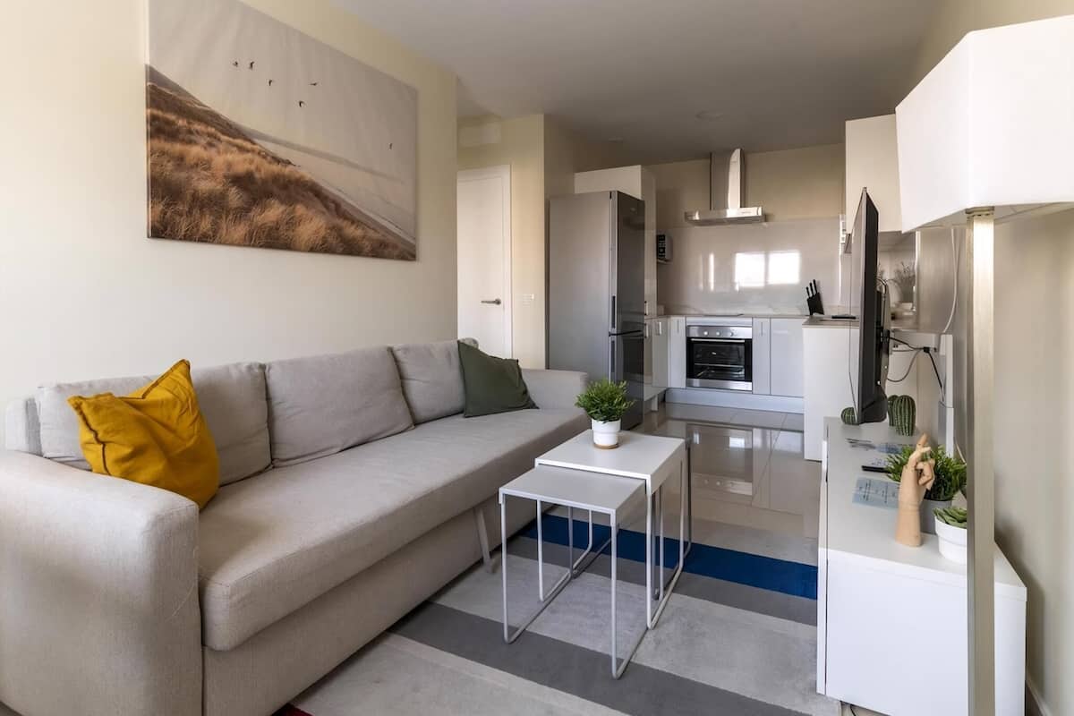 A modern living room with a sofa, a coffee table, and a kitchen in the background.