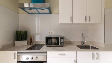 Una cocina moderna con armarios blancos, horno empotrado, microondas, lavaplatos y una campana extractora azul.