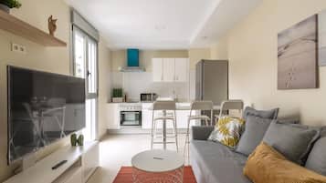 Una sala de estar moderna con televisor, sofá y un comedor con sillas y una mesa.