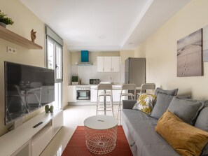 A modern living room with a TV, sofa, and a dining area with chairs and a table. - Guestready - Nuevos Livian Suites Las Palmas (Las Palmas de Gran Canaria)