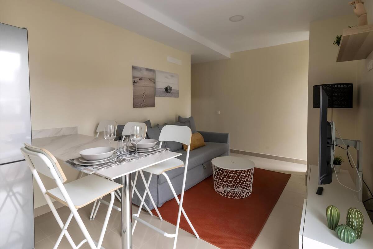 A modern living space with a dining area, a sofa, a TV, and a small plant.