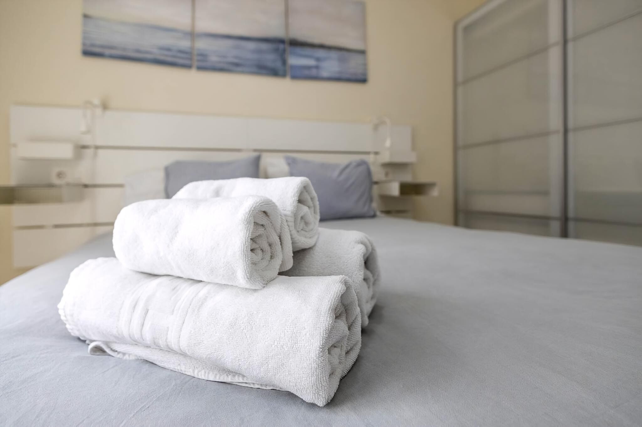 Una cama bien hecha, toallas blancas enrolladas, una mesita de noche con lámpara y vista al mar a través de una ventana.