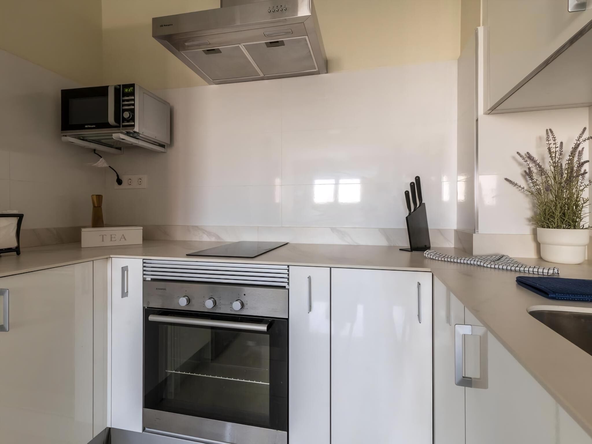 Una cocina moderna con electrodomésticos de acero inoxidable, horno empotrado, microondas y una zona de té.