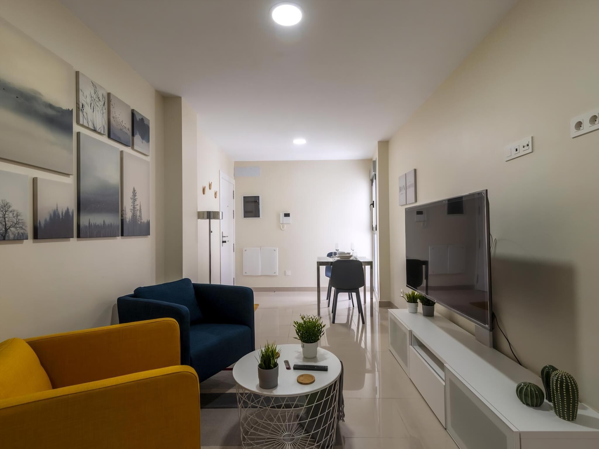 A modern living room with a sofa, a coffee table, a TV, and a dining area with chairs.