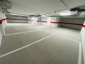 Eine mehrstöckige Parkgarage mit weißen Wänden und roten Akzenten, mit zahlreichen Stellplätzen und Notausgängen.