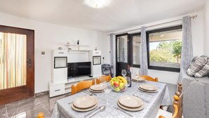 Un coin repas avec une table dressée pour quatre personnes, un téléviseur et un canapé avec des coussins.