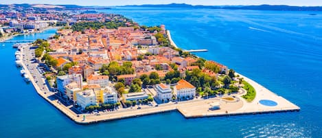 Vista aérea de un pueblo costero con puerto deportivo, edificios y un mar azul cristalino.