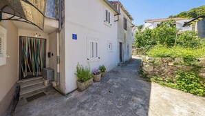 Une rue étroite avec un bâtiment blanc, des marches en pierre et des plantes en pot.