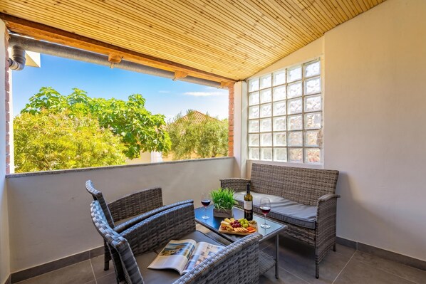 Ein Balkon mit Korbmöbeln, einem Tisch mit Flasche und Gläsern sowie einer Zeitschrift.