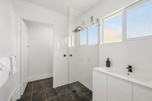 Un bagno moderno con box doccia in vetro, lavabo bianco e finestra che permette l'illuminazione naturale.