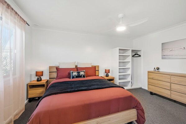 Una camera da letto con un letto, comodini, un armadio, una ventola a soffitto e un quadro appeso al muro.