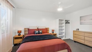 A bedroom with a bed, bedside tables, a wardrobe, a ceiling fan, and a painting on the wall.