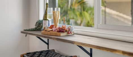 A wooden table with a variety of food items and a bottle of wine, positioned near a window with a view of greenery.