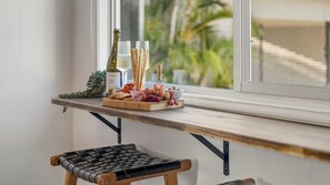 A wooden table with a variety of food items and a bottle of wine, positioned near a window with a view of greenery.