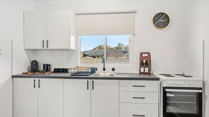 A modern kitchen with white cabinets, a window with a view, a clock, and a wine cooler.