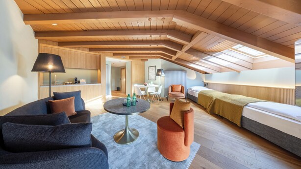 Habitación tipo loft con techo alto, comedor y una zona de estar acogedora con sofá y reposapiés.
