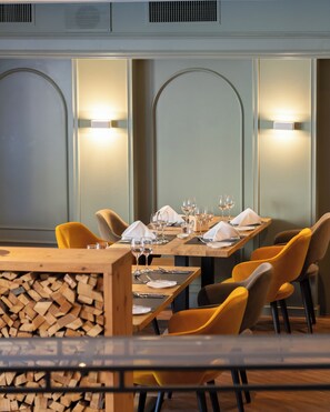 Interior de restaurante con mesas de madera, sillas amarillas e iluminación en la pared.