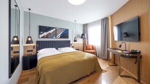 Habitación de hotel moderna con cama, mesitas de noche, un escritorio con silla, televisor y una obra de arte en la pared.