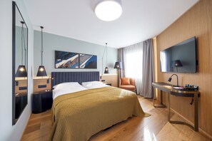 Habitación de hotel moderna con cama, mesitas de noche, un escritorio con silla, televisor y una obra de arte en la pared.