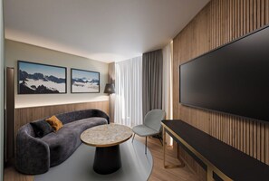 Una habitación de hotel moderna con un sofá, una mesa redonda, un televisor y cuadros enmarcados en la pared.