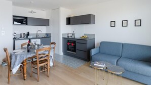 A modern kitchen with a dining area, a blue sofa, and a small side table. - Apartment in Porspoder Near Plage du Bourg (Porspoder)