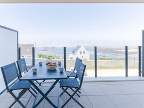 Ein Balkon mit Tisch und Stühlen, einem Brotkorb und Blick auf das Meer und Gebäude.