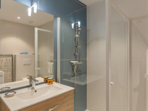 Ein Badezimmer mit Duschkabine aus Glas, einem weißen Waschbecken mit Spiegel und einem hölzernen Waschtisch.