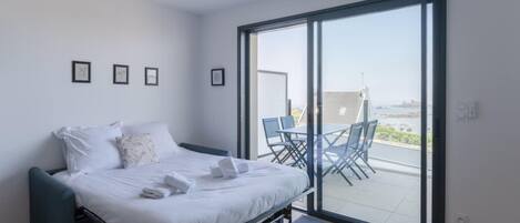 A modern bedroom with a bed, a small table, and a view of the outdoors through a sliding glass door.