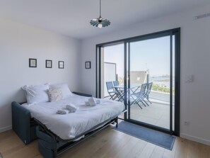 Ein modernes Schlafzimmer mit einem Bett, einem kleinen Tisch und Blick ins Freie durch eine Schiebetür.