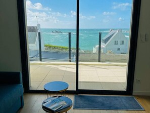 Ein Zimmer mit einer großen Glasdoor zu einem Balkon mit Blick auf das Meer und Gebäude.