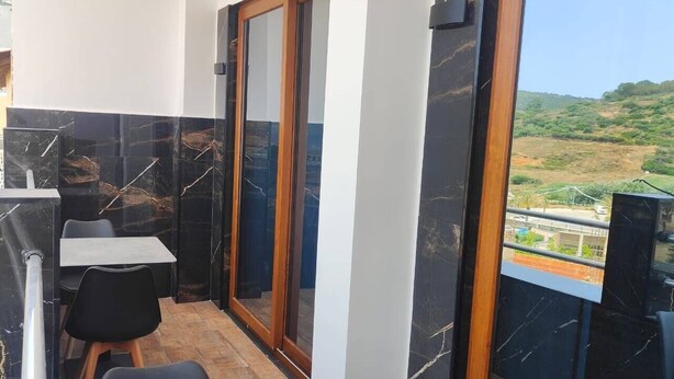 Un balcón con una mesa y sillas, una puerta corrediza de vidrio y vistas a zonas verdes.
