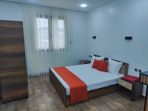 Ein Schlafzimmer mit einem Bett, Nachttischen, einem Holzschrank und einem Fenster mit Vorhängen.