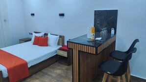 Habitación de hotel con una cama, un escritorio con una silla, una mesita con una botella y un televisor instalado en la pared.