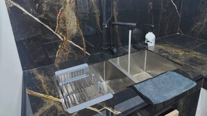 Una cocina con un lavamanos de acero inoxidable, un escurreplatos y una manguera negra.