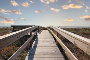 Une promenade en bois menant à une plage, avec un ciel dégagé.