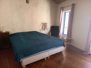 A room with a bed, a chair, a small table, and a window with curtains. - Authentic and charming village house with a view of the garrigue (Fitou)