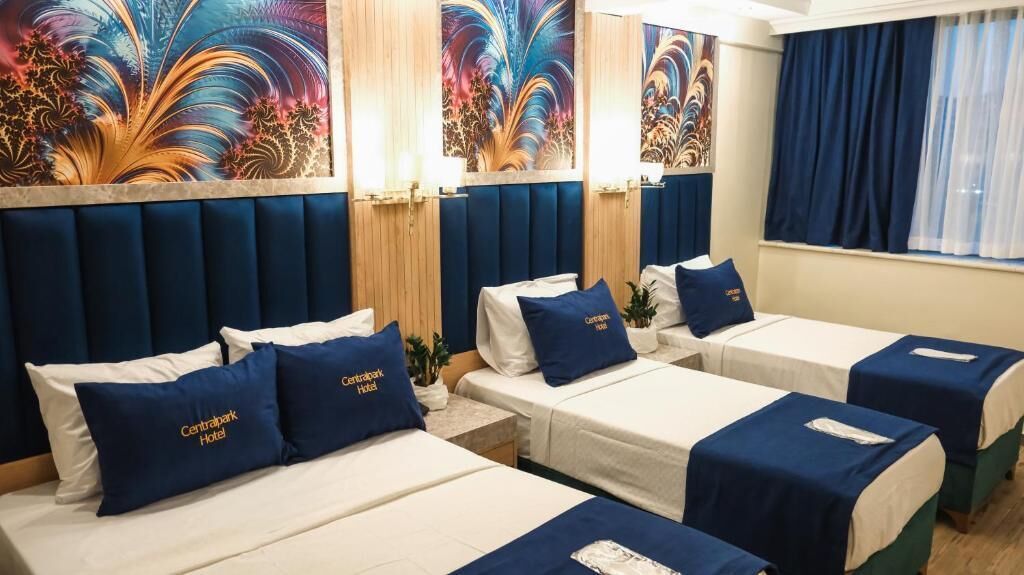 A hotel room with four beds, each with a blue pillow and a white bedspread. The room has a wooden headboard and a large window with blue curtains.