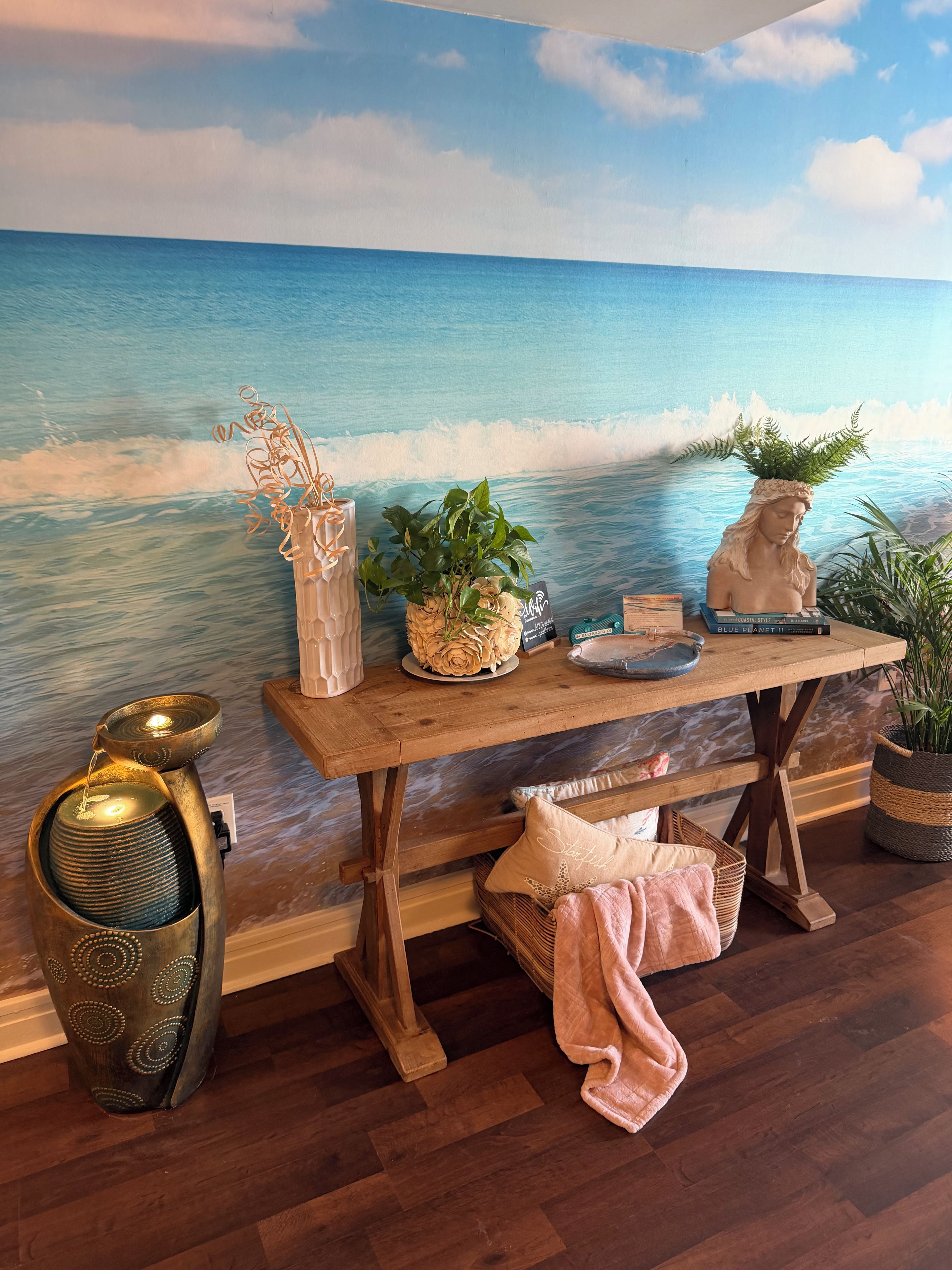 Un tavolo di legno con oggetti decorativi, un affresco che raffigura l'oceano e una lampada da terra.