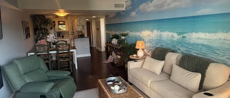 A living room with a sofa, a green chair, a coffee table, and a wall mural of the ocean.