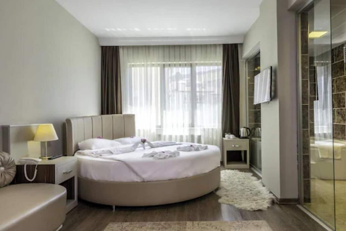 A modern hotel room with a round bed, a sofa, a TV, and a glass shower enclosure.