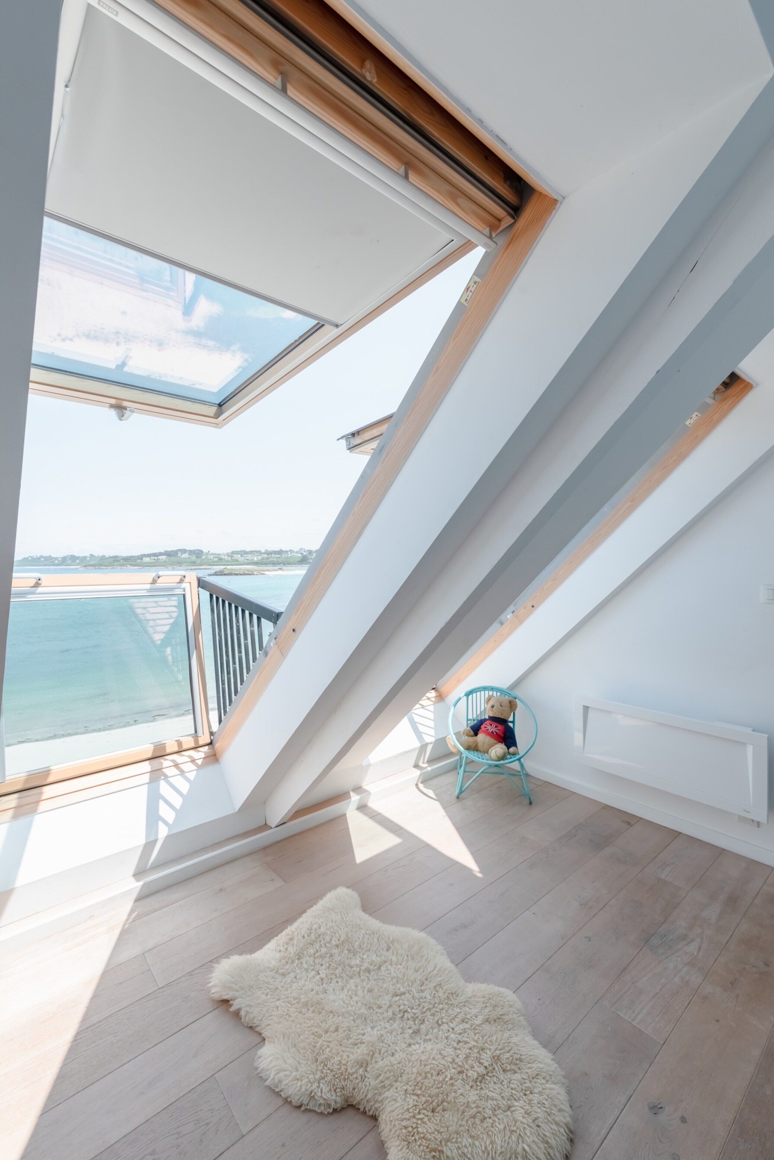 A high-ceilinged room with skylights, a wooden floor, and a view of the sea.
