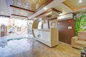 A reception area with a marble floor, a reception desk, a wall-mounted air conditioner, and a fan. - Townhouse Oak Iskcon Jaipur Formerly Olive Greens (Jaipur)