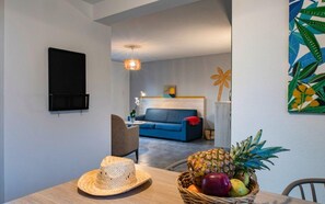 A modern living room with a blue sofa, a dining table with a fruit basket, a hat, and a TV mounted on the wall. - Fabregues Villa With Shared Pool (Fabregues)