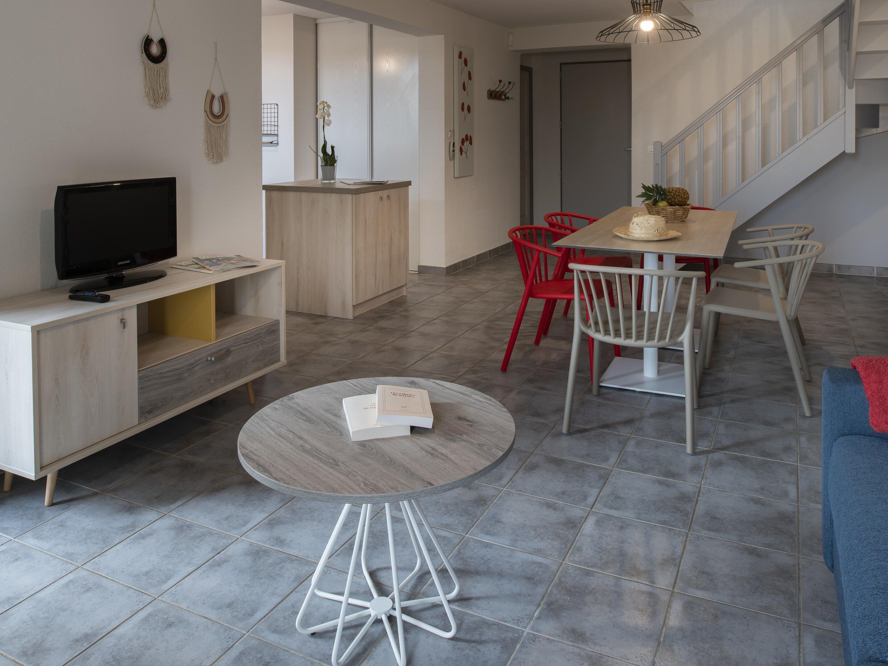Una sala de estar moderna con televisor, una mesa de centro redonda y un comedor con sillas rojas.