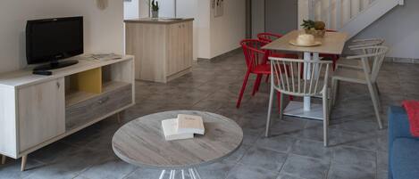 Una sala de estar moderna con televisor, una mesa de centro redonda y un comedor con sillas rojas.