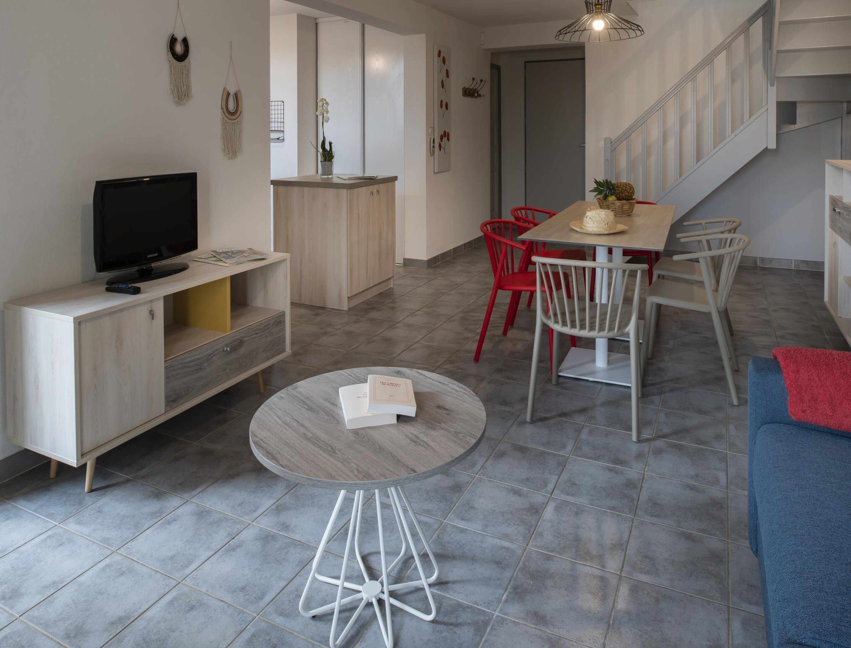 A modern living space with a flat-screen TV, a round coffee table, a dining table with chairs, and a staircase.