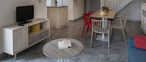 A modern living space with a flat-screen TV, a round coffee table, a dining table with chairs, and a staircase.