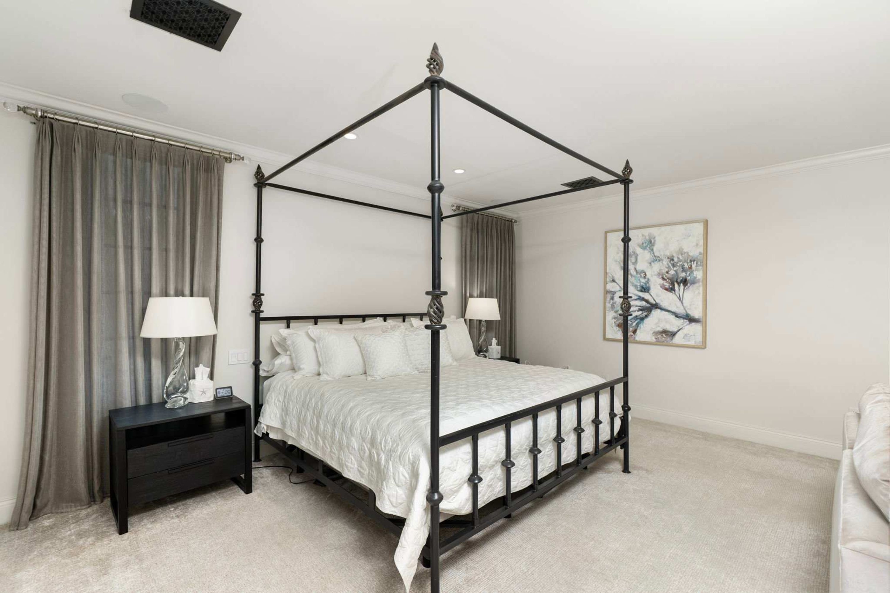A four-poster bed with a black frame, a bedside table with a lamp, and a painting on the wall.