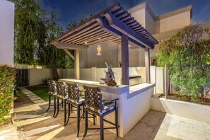 Ein Außenbereich mit Küche, einer Pergola, einer Theke und Sitzgelegenheiten.